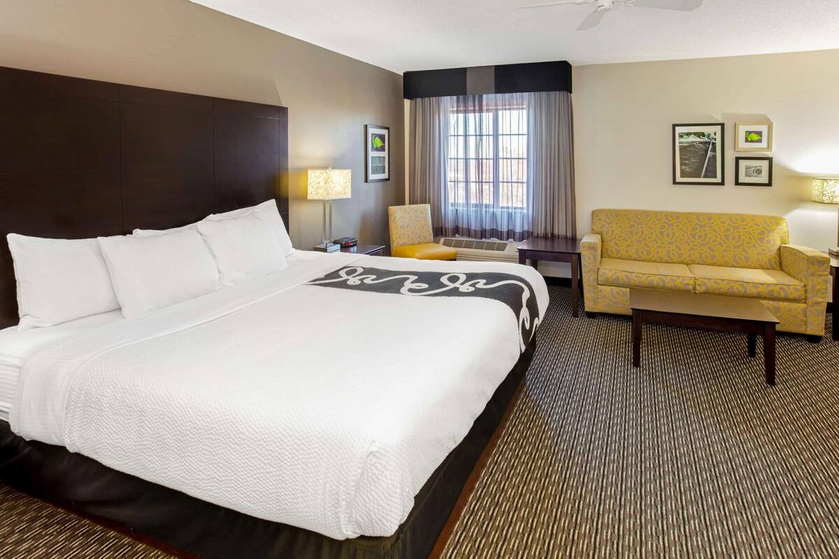 A hotel room with a large bed, a sofa, a chair, a desk, and a window with curtains.