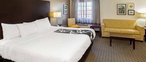 A hotel room with a large bed, a sofa, a chair, a desk, and a window with curtains.