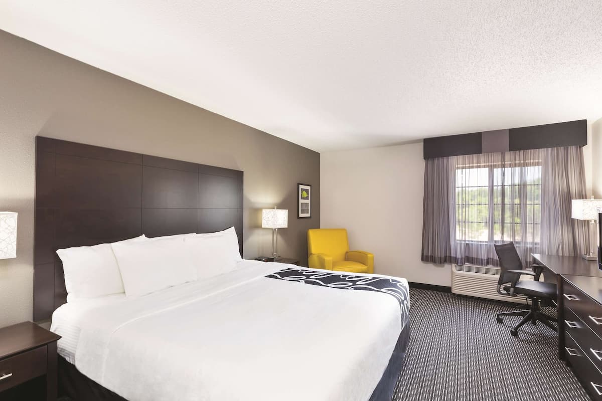 A hotel room with a large bed, a desk, a chair, and a window with curtains.