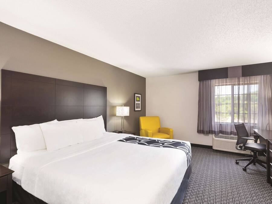 A hotel room with a large bed, a desk, a chair, and a window with curtains.