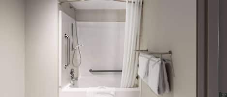 A modern bathroom with a bathtub, shower, and handrails.