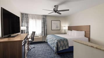 Una habitación de hotel con cama, escritorio, televisión y ventilador de techo.