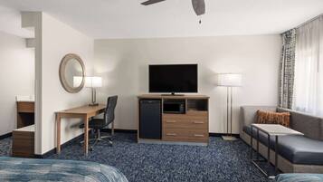 A hotel room with a bed, a desk, a television, a sofa, and a ceiling fan.