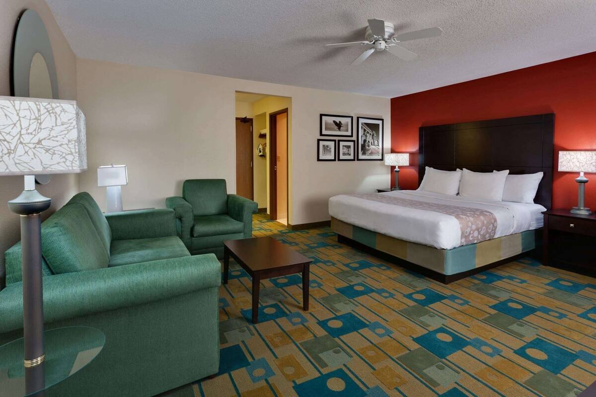 A hotel room with a bed, two armchairs, a coffee table, a ceiling fan, and a patterned carpet.