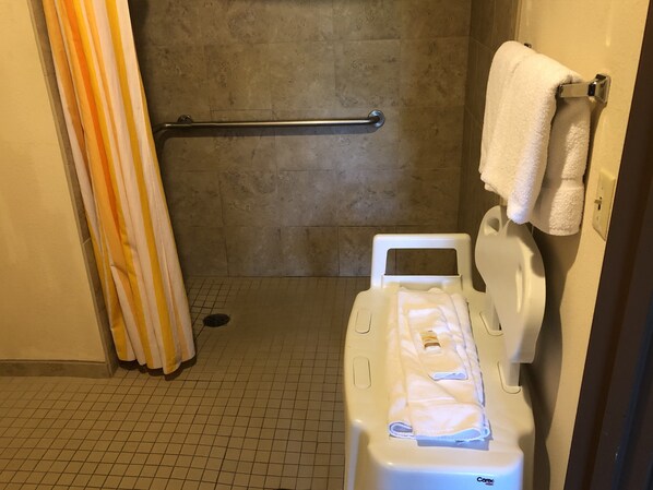 Un baño con ducha, barra de apoyo, inodoro y perchero.