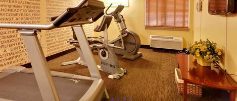 A hotel room with a treadmill, an exercise bike, a dining table with a vase of flowers, and a wall with motivational quotes.