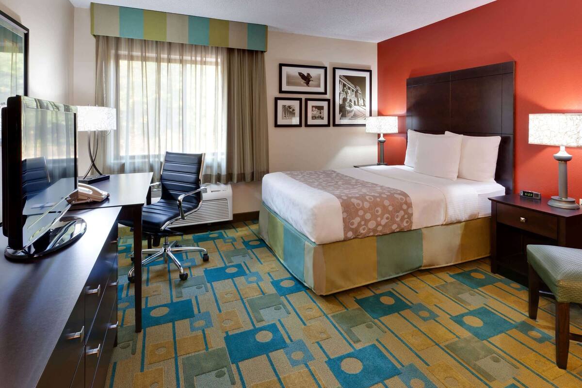A hotel room with a bed, desk, chair, and a television.