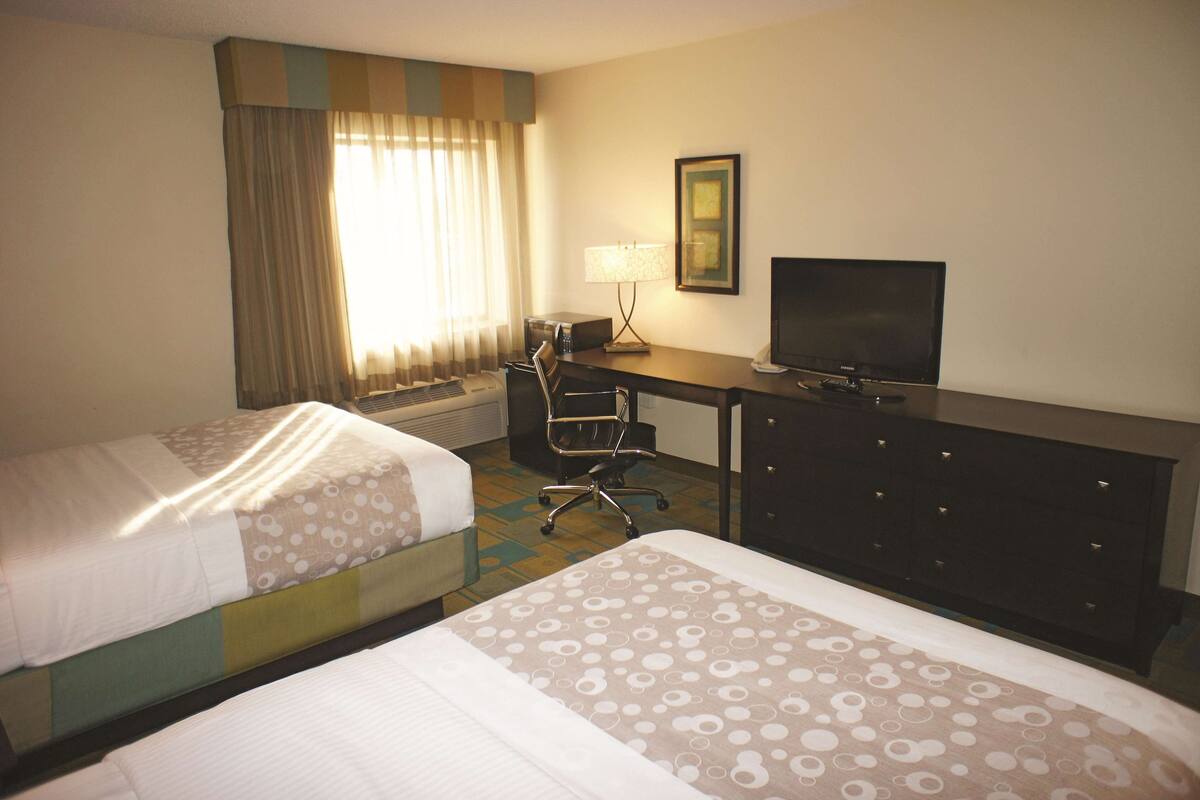 A hotel room with two beds, a desk with a television, a chair, and a lamp.