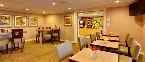 A hotel dining area with multiple tables and chairs, a coffee station, and framed artwork on the walls.