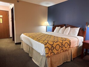 A hotel room with a bed, a nightstand, a lamp, and a door. - Baymont by Wyndham Corydon (Corydon)