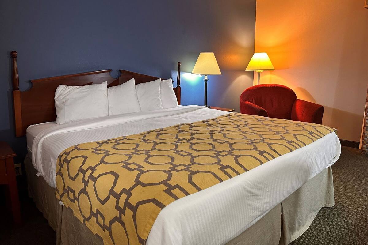 A hotel room with a wooden bed, a red chair, and two bedside lamps.