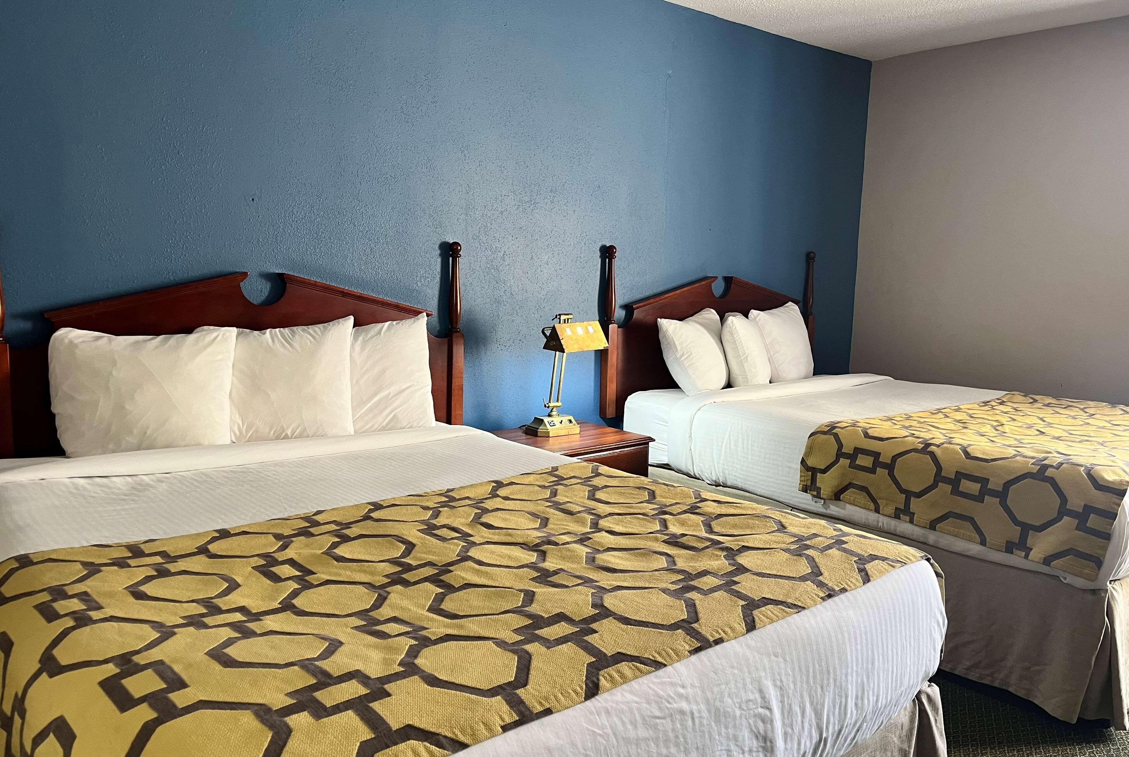A hotel room with two beds, each with a wooden headboard, white bedding, and a patterned bedspread.