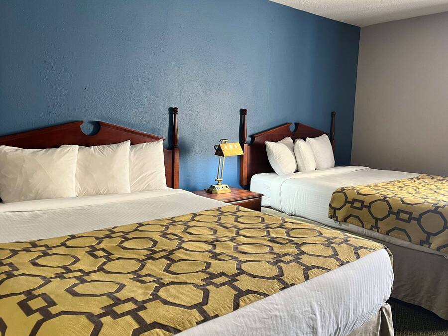 A hotel room with two beds, each with a wooden headboard, white bedding, and a patterned bedspread.