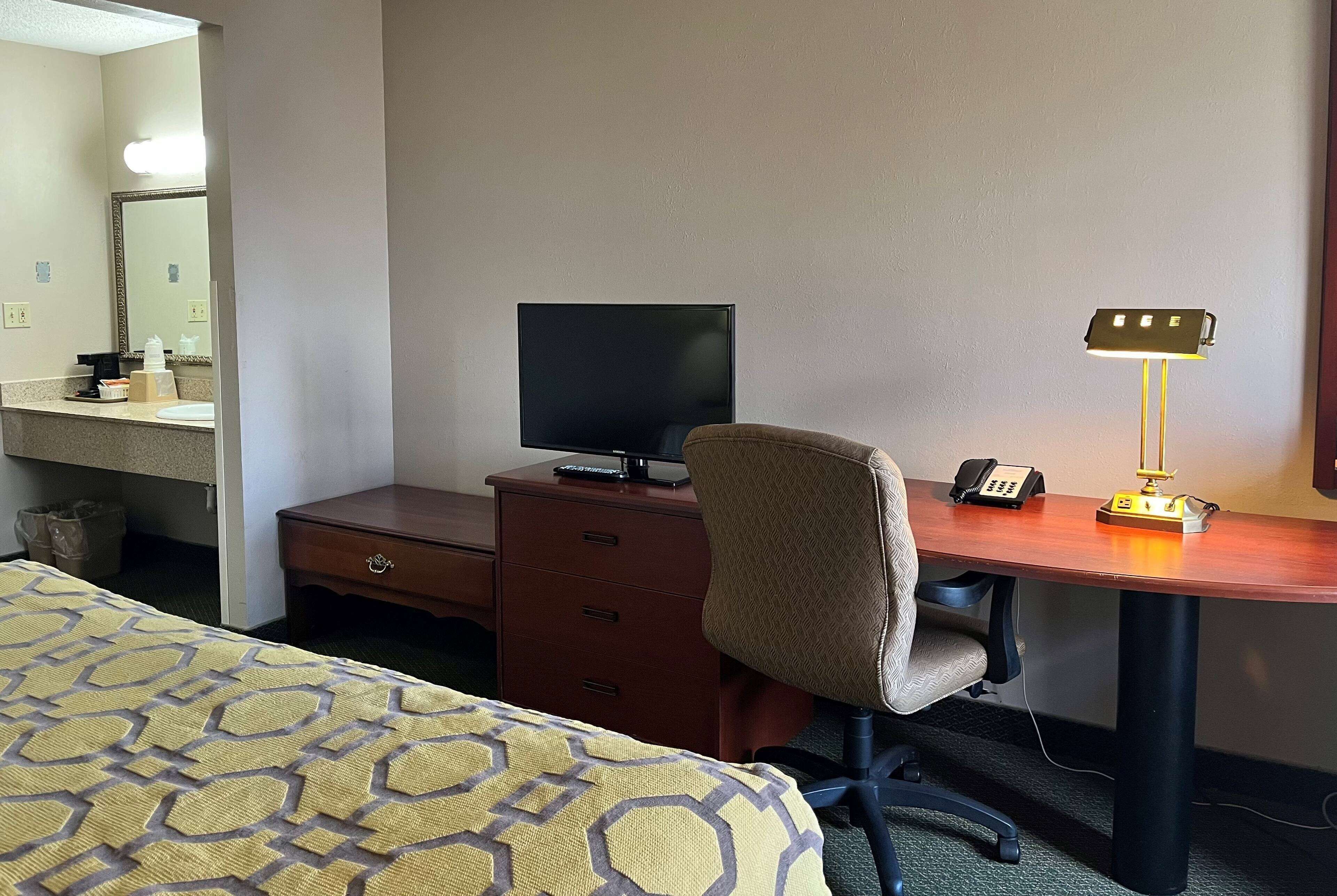 A hotel room with a bed, a desk with a computer monitor, a lamp, and a telephone.