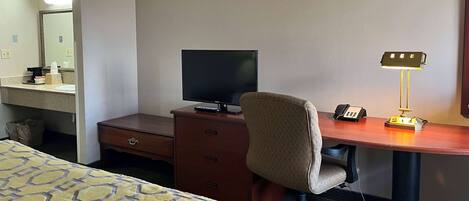 A hotel room with a bed, a desk with a computer monitor, a lamp, and a telephone.
