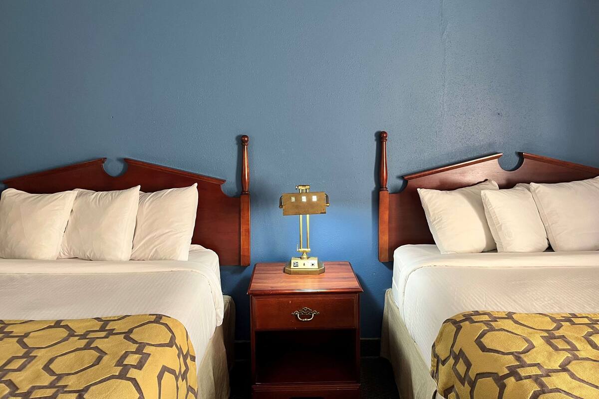 A hotel room with two beds, a nightstand with a lamp, and a wooden headboard.