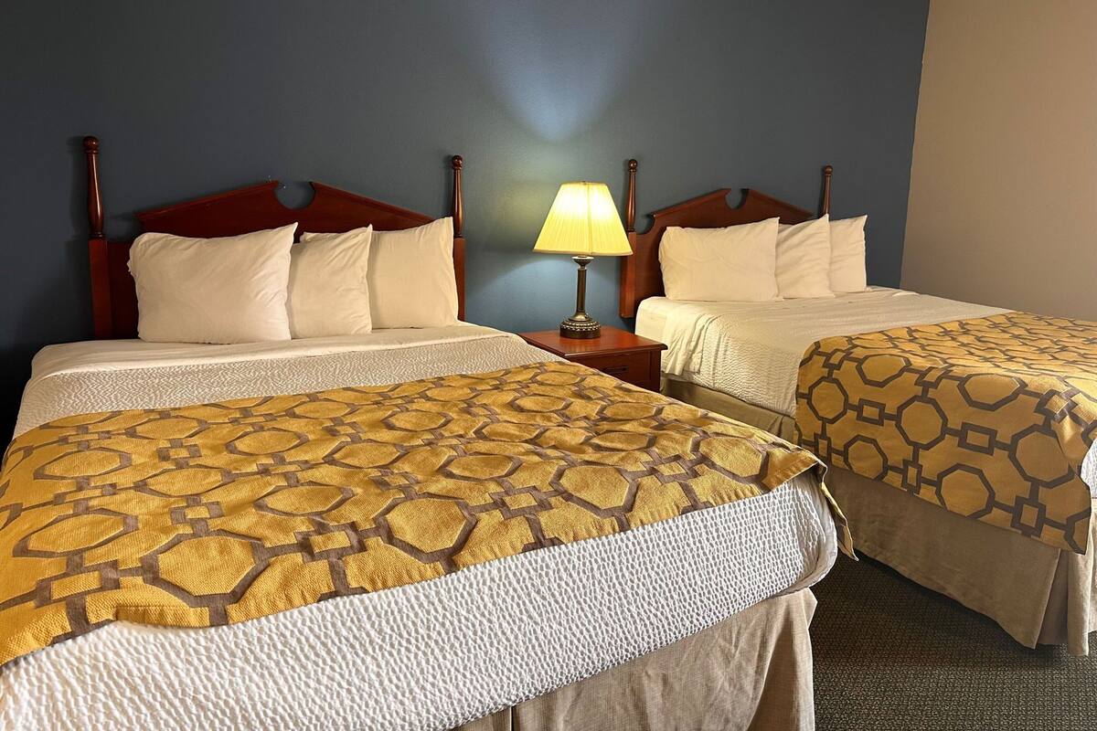 A hotel room with two beds, a nightstand with a lamp, and a blue wall.