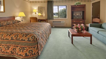 A hotel room with a large bed, a desk with a lamp, a television, a sofa, and a window with a view of trees.