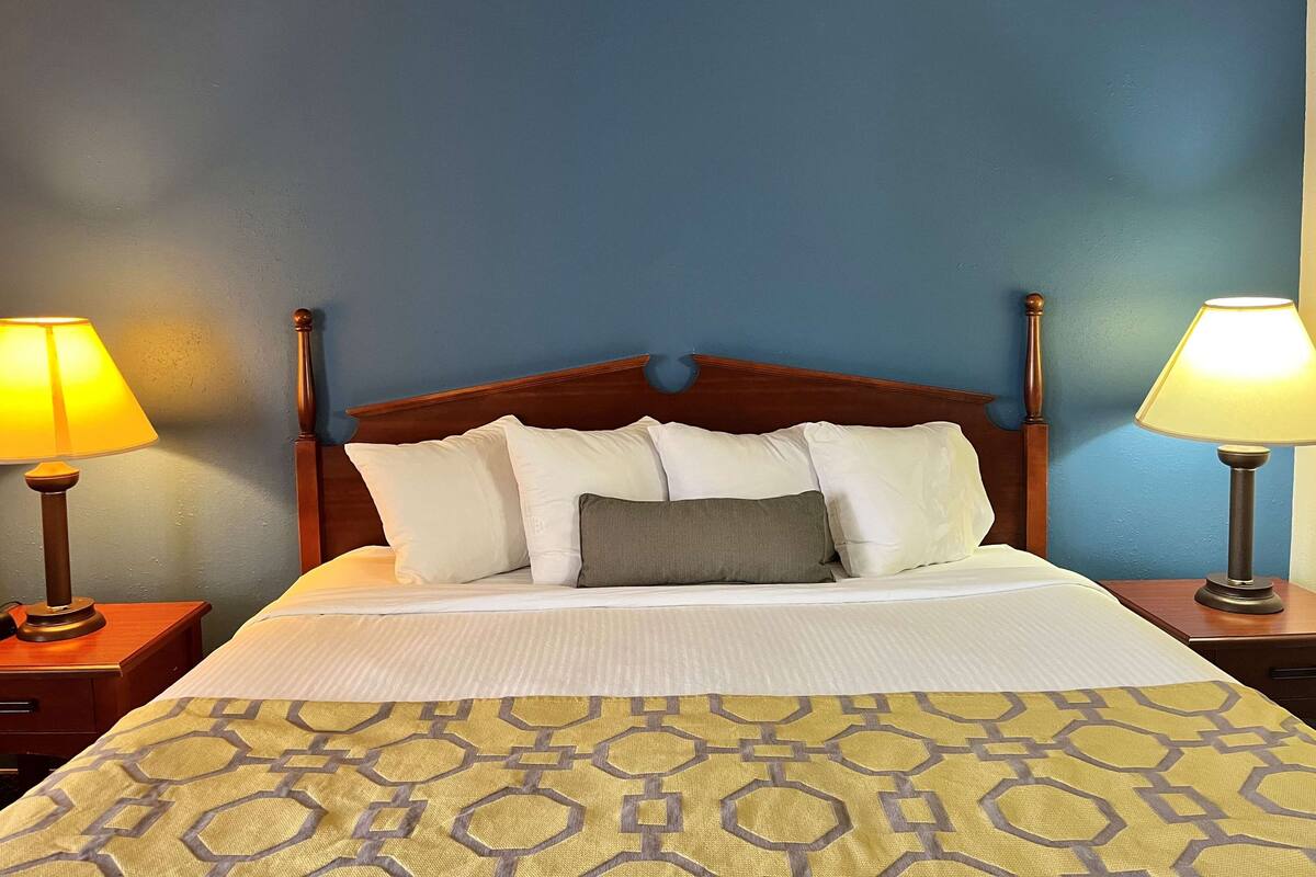 A neatly made bed with a patterned bedspread, two bedside lamps, and a wooden headboard.