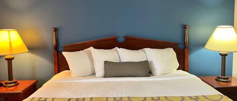 Una cama bien hecha con un edredón estampado, dos lámparas de noche y un cabecero de madera.