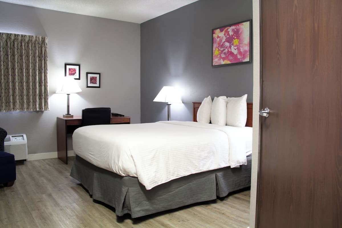 A hotel room with a bed, bedside lamps, a desk, and a chair.