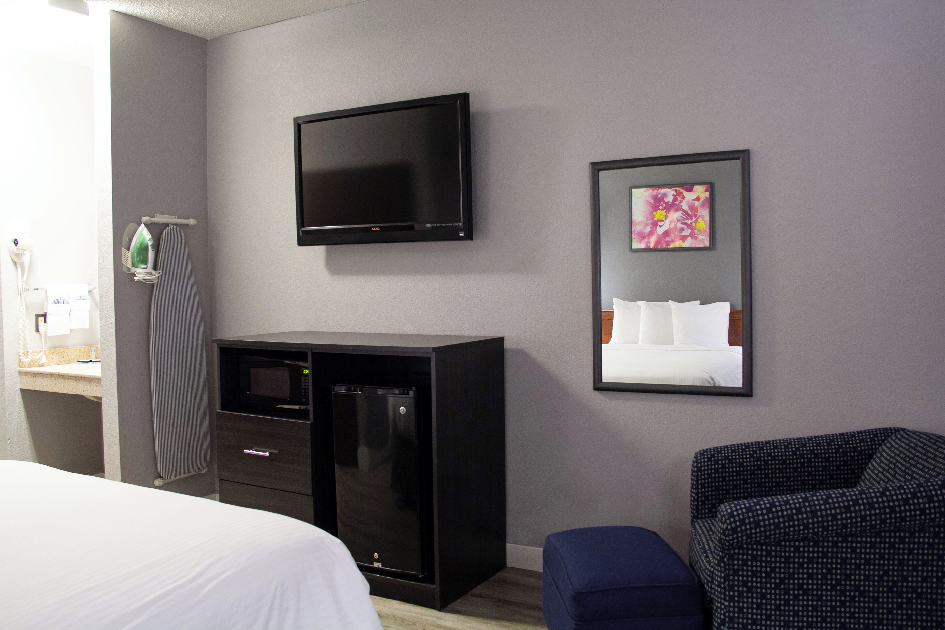 Une chambre d’hôtel comprenant un lit, un téléviseur à écran plat fixé au mur, un four à micro-ondes, un petit meuble, une chaise et un tableau encadré au mur.