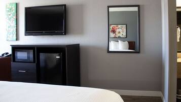 Habitación de hotel con cama, televisor montado en la pared, microondas, refrigerador y espejo que refleja parte del cuarto.