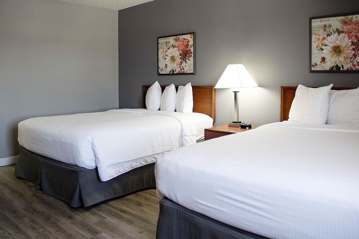 A hotel room with two single beds, a nightstand with a lamp, and floral artwork on the walls.