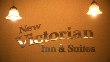 Señal del New Victorian Inn & Suites con un fondo texturizado y dos lámparas colgantes.