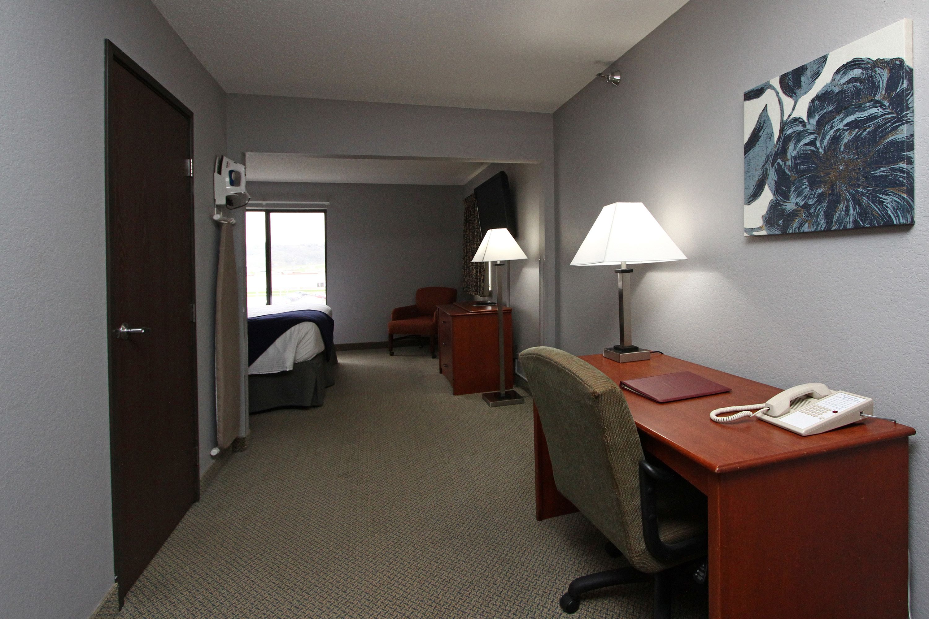 A hotel room with a bed, desk, chair, lamp, phone, and artwork on the wall.
