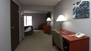 A hotel room with a bed, desk, chair, lamp, phone, and artwork on the wall.