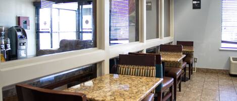 A restaurant interior with marble-topped tables and wooden chairs, a cash register, and a window with blinds.