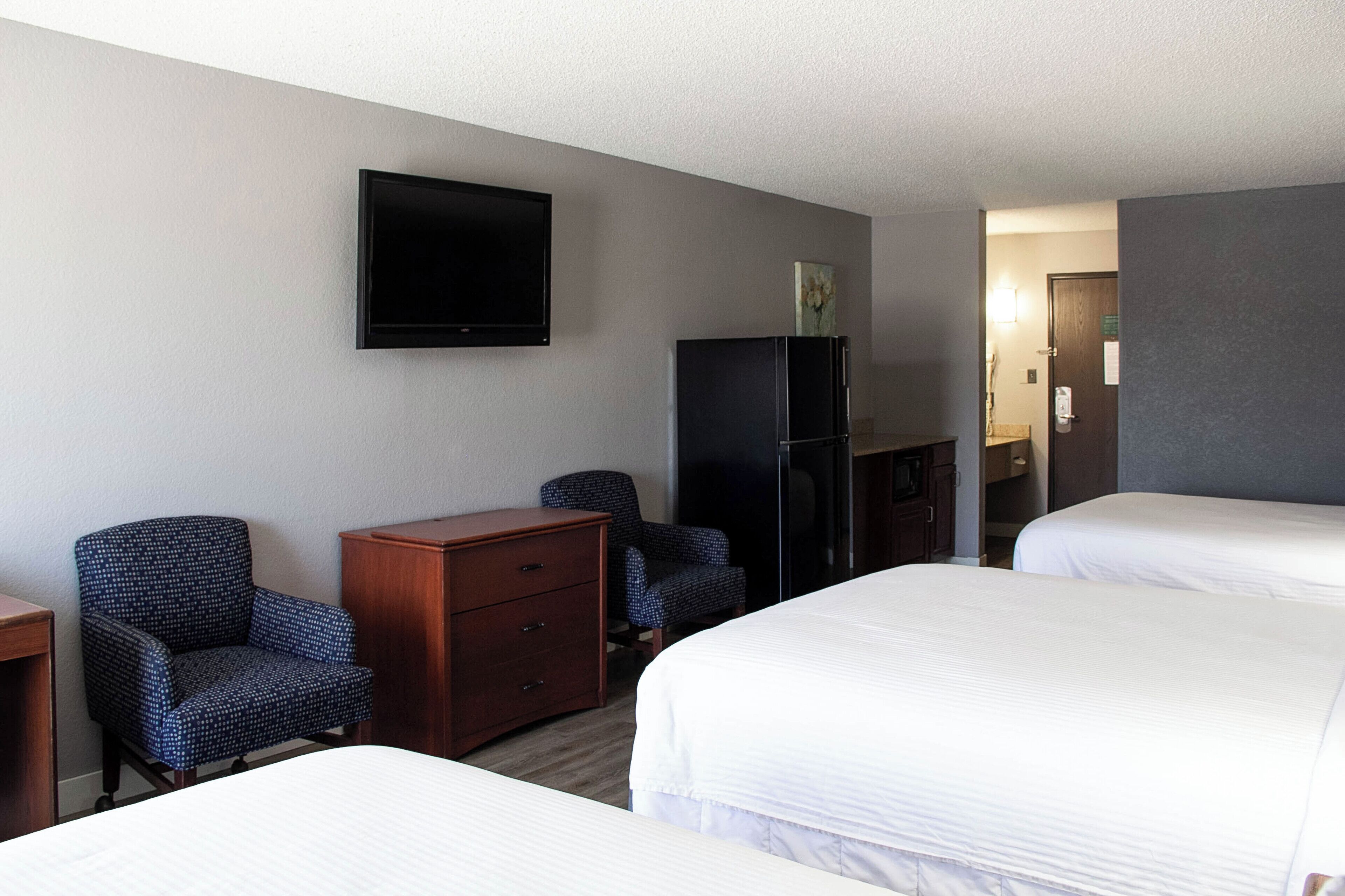A hotel room with two beds, a flat-screen TV mounted on the wall, a wooden dresser, and a refrigerator.