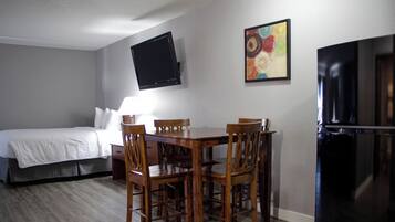 Habitación de hotel con cama, una mesa de comedor con sillas, un televisor de pantalla plana en la pared, un refrigerador y un cuadro.