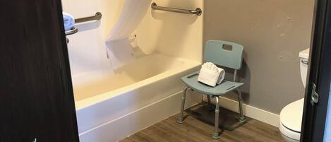 A bathroom with a bathtub, a shower curtain, a toilet, and a chair.