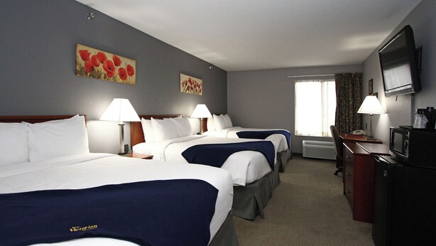 Quarto de hotel com três camas, uma escrivaninha, uma televisão e duas pinturas na parede.