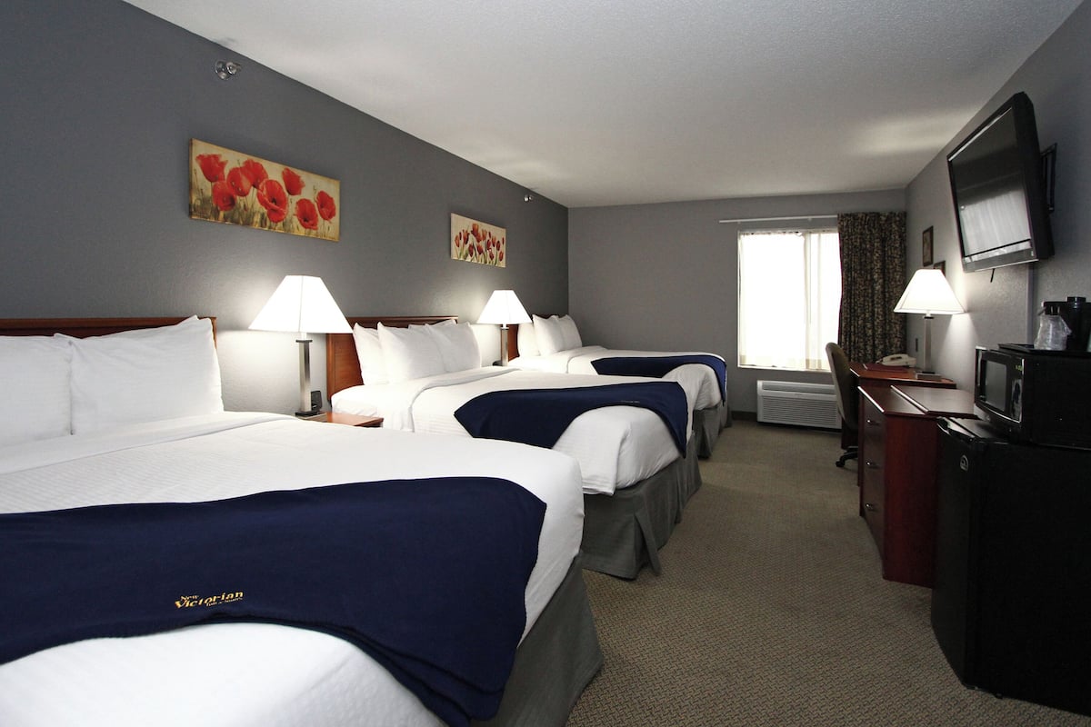 A hotel room with three beds, a desk, a television, and two paintings on the wall.