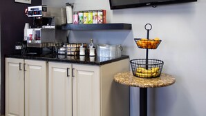 Cozinha com máquina de café, cesta de frutas e prateleira com cápsulas de café.