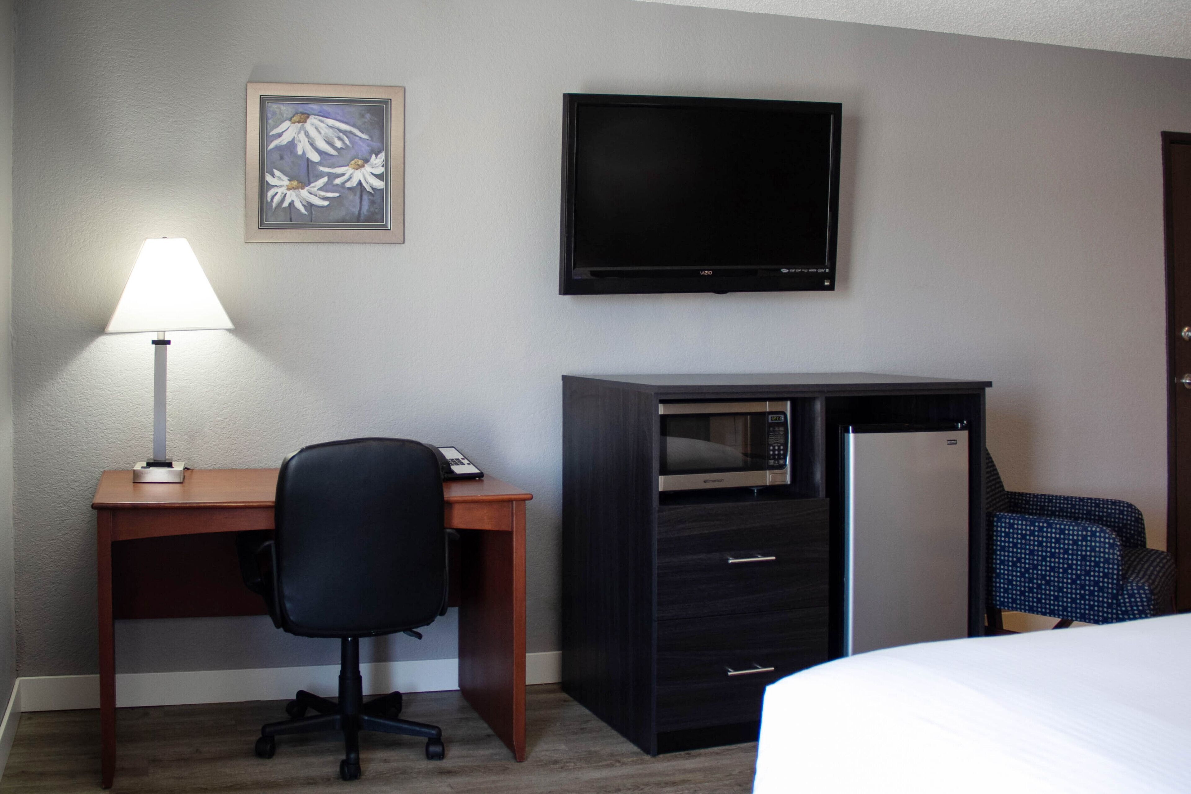 A hotel room with a desk, a chair, a bed, a TV, a microwave, and a refrigerator.