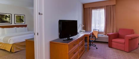 Habitación de hotel con una cama, un televisor sobre un aparador de madera, un escritorio con una silla y un sillón rojo.