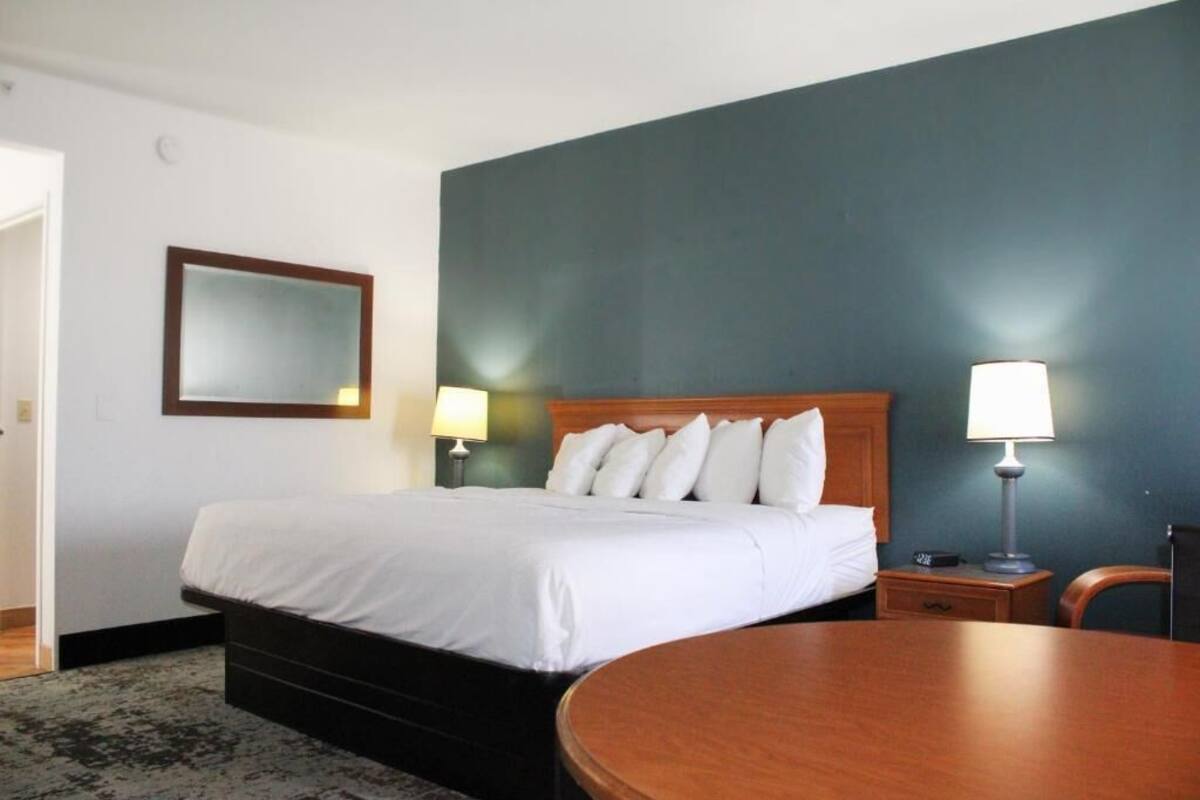 A hotel room with a bed, bedside lamps, a round table, and a mirror on the wall.