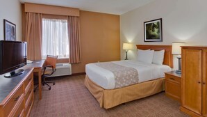 A hotel room with a bed, a desk with a television, a chair, a lamp, and a wardrobe. - La Quinta Inn & Suites by Wyndham Lakeland East (Lakeland)