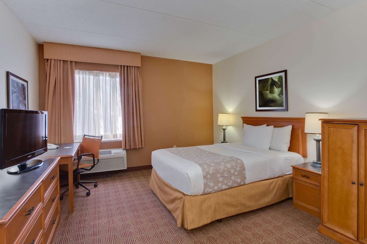 A hotel room with a bed, a desk with a television, a chair, a lamp, and a wardrobe.