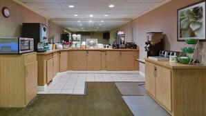 A hotel kitchen with wooden cabinets, a microwave, a coffee machine, and a clock on the wall. - La Quinta Inn & Suites by Wyndham Lakeland East (Lakeland)