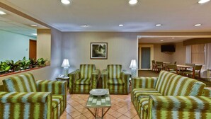 A hotel lobby with patterned sofas, a glass coffee table, and a dining area with chairs and a TV. - La Quinta Inn & Suites by Wyndham Lakeland East (Lakeland)