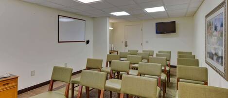 Uma sala de conferências com fileiras de cadeiras, um quadro branco, uma televisão e um quadro na parede.