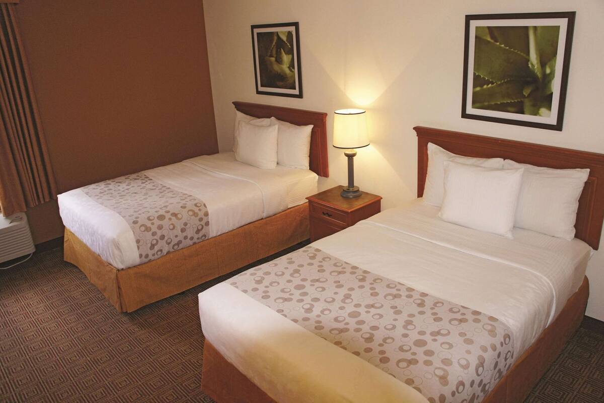 Two adjacent hotel beds with matching headboards, a bedside table with a lamp, and two framed pictures on the wall.