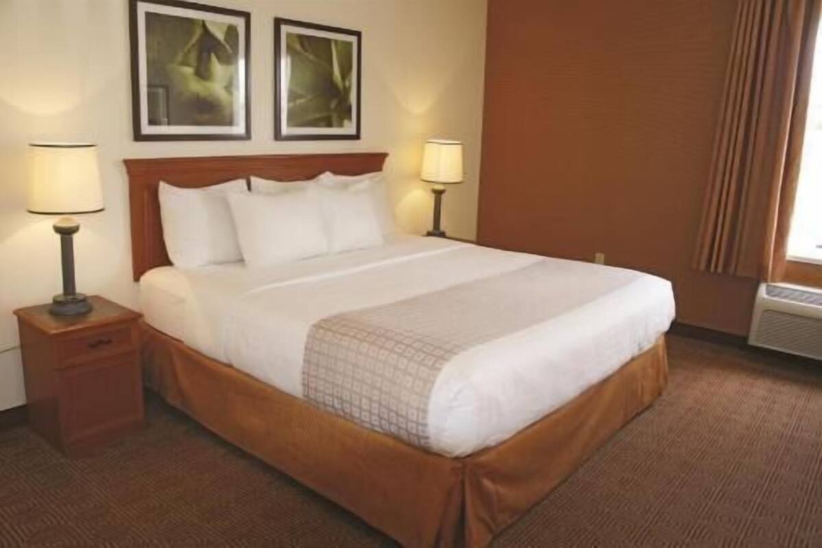 A hotel room with a large bed, two bedside lamps, a wooden headboard, and two framed pictures on the wall.