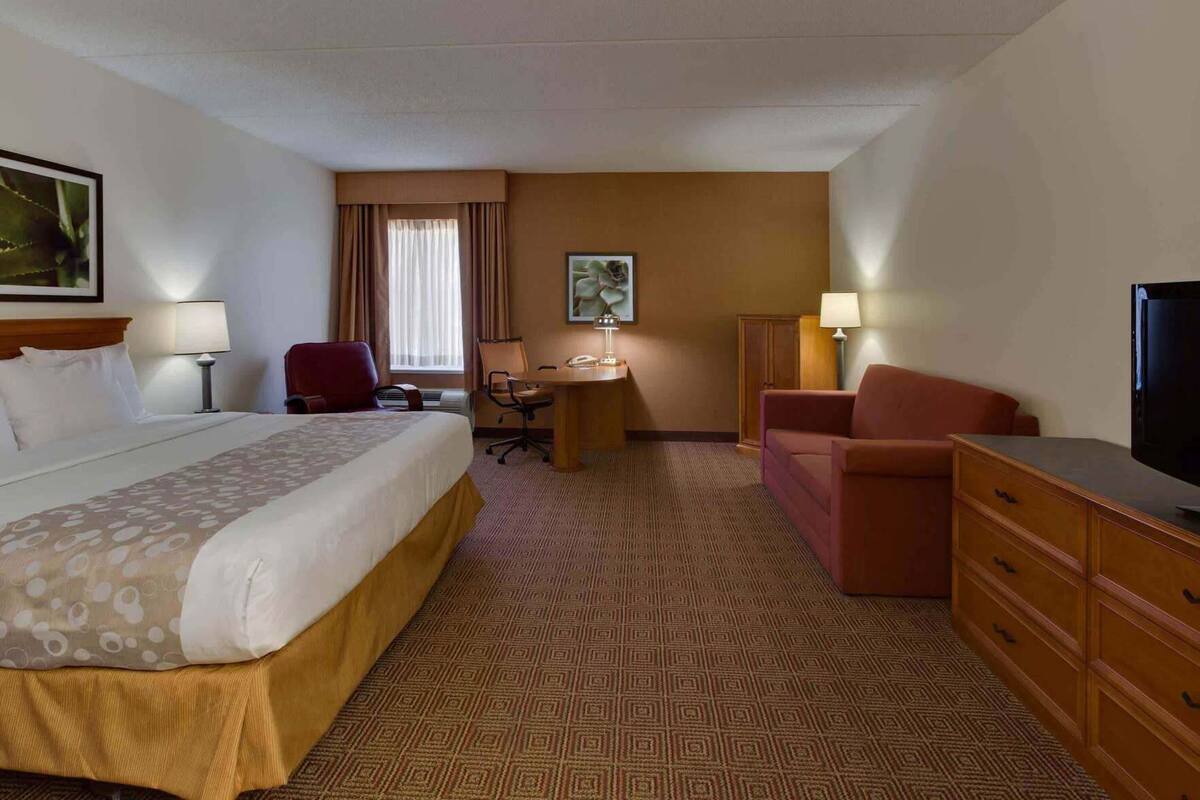 A hotel room with a bed, desk, chair, television, and a dresser.