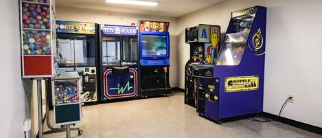 Una habitación con juegos de arcade, una máquina expendedora de bolas de colores y un carrito con dispensador de bebidas.